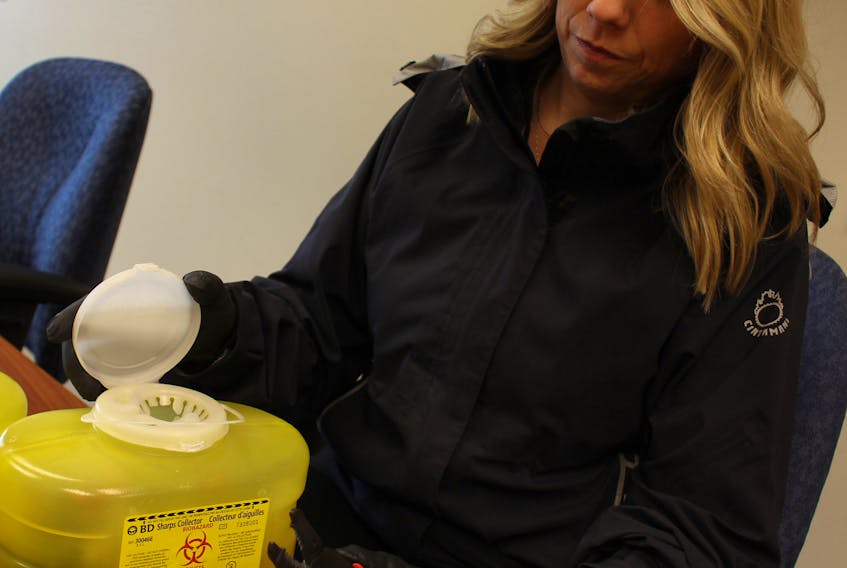 Cpl. Jennifer Driscoll examines needles that have been disposed of in a sharps container. Driscoll says consistent reporting of when used needles are found in public spaces can help police determine areas of drug activity.