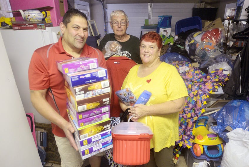 Santa’s Angels president Kenny Zakem, left, Gifts from the Heart founder Betty Beggs-Brooks, right, and her husband, Rob Brooks, display some of the donations that are currently being stored in Beggs-Brooks’ home. The two charities are teaming up in hopes of reaching more Islanders in need and finding a warehouse that can be used to store donations.