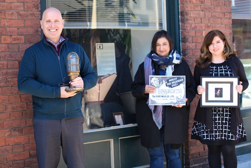 Charlottetown Coun. Greg Rivard, chairman of the planning and heritage committee, holds a ship’s light converted into a table lamp, while Linda Berko, centre, curator of collections and conservator at the P.E.I. Museum and Heritage Foundation, holds a 1937 advertisement for the Pure Milk Company and while Natalie Munn, heritage researcher and collections co-ordinator for the city, holds a sign for the exhibit entitled Queen Charlotte’s Curiosities. The display is located along the storefront windows of the planning and heritage department at 233 Queen St.
