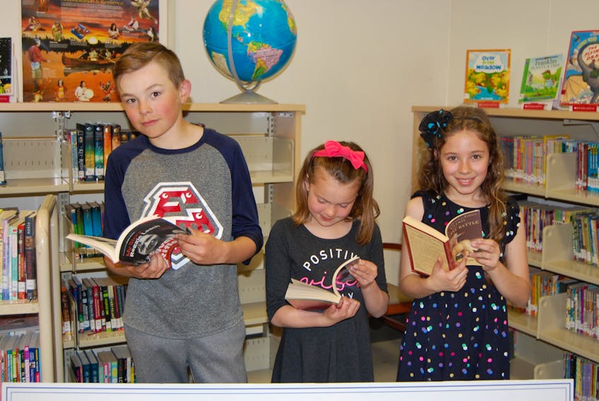 Cayle Coffin, 11, Serenity Jadis, 8, and Clara Ezekiel, 9, look over some of the new books in the Mount Stewart Consolidated School library on May 31, which were purchased thanks to a literacy grant from Indigo.