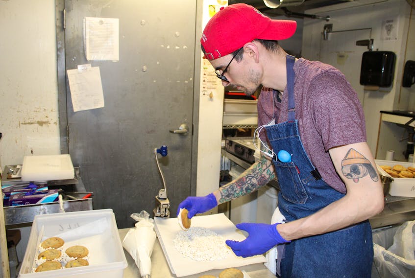 Next Level Cookie owner Jordan Cameron adds popcorn crumble to a cookie sandwich made with M&M cookies and vanilla buttercream, which he calls the Blockbuster, in the Merchantman restaurant’s prep kitchen.
