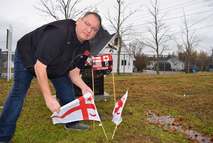 Millbrook band councillor Colin Bernard shows the new grave markers that have been placed in front of headstones of the community’s war veterans prior to Friday, when a group of preschoolers will be arriving to place Mi’kmaq flags in front of each. At right is one of the many banners posted in the community to honour veterans.