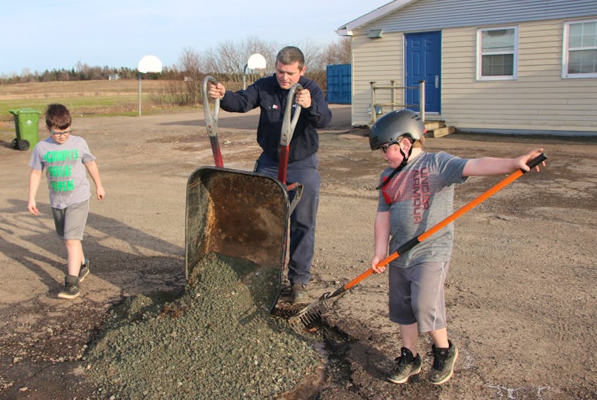 Arnold Stewart and his sons Kaden, left, and Bryson spent an evening filling holes in the driveway of North River Elementary School with gravel. Some of the holes were deep enough that people were afraid to drive through them.