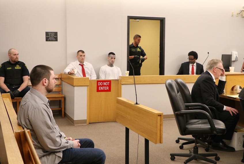 Tyler Donahue, 24 (grey shirt, foreground), and sitting in the prisoners’ dock (from left) Gary Hennessey, 33, Mitchell Nippard, 26 and Abdifatah Mohamed, 28, wait for their trial to resume at provincial court in St. John’s Wednesday.