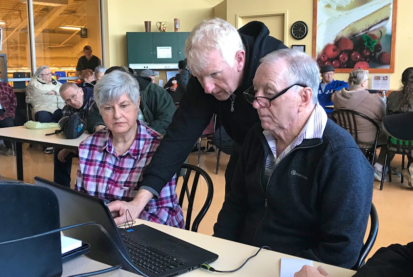 Edith Avery, left, has her tax return completed by volunteer Ken Snell, right, as Allan Murray has a look at the work at the tax clinic inside New Glasgow Atlantic Superstore on Tuesday.