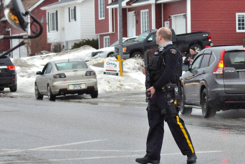 An RCMP officer carrying a rifle in his hands watches traffic as students at Stephenville High School were being released following a threat and lockdown at the school Friday.
