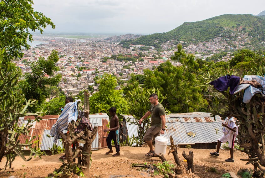 Ash Buckle carries a bucket of water through the hillside town of Calvaire, which overlooks the larger city of Cap-Haïtien, seen in the background.