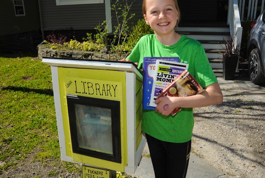 Jane Tucker, 11, poses for a photo with the little free lawn library her family has established on the curb outside their home on Central Street in Corner Brook.