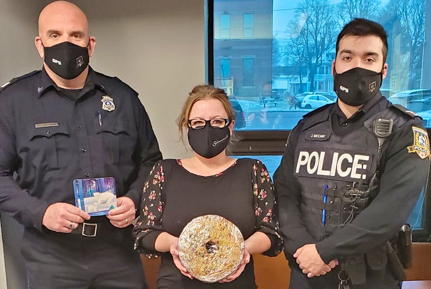 Sgt. Jason Blacquiere, left, Tanya Yeo-Campbell and Cst. Jesse McCabe pose with the Waite Fruitcake, mailed from Bedford, Nova Scotia.