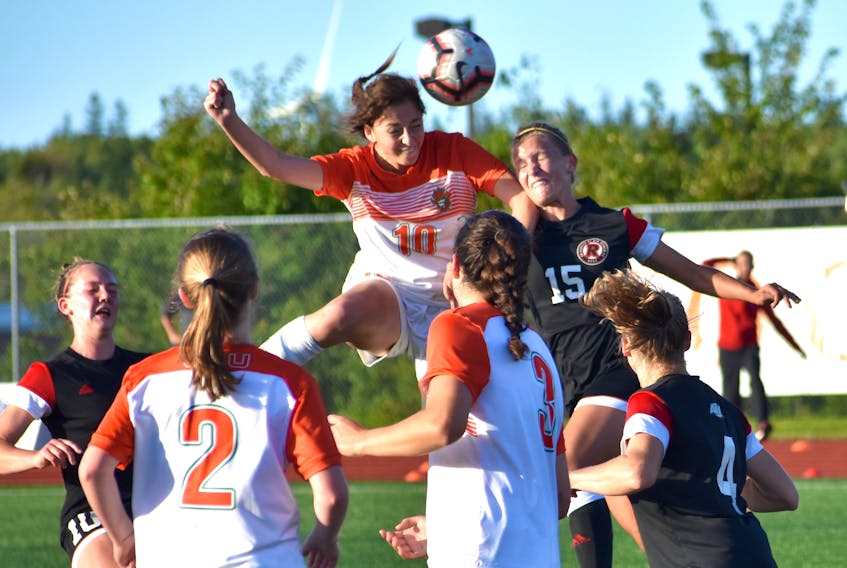 Amelia Carlini of the Cape Breton Capers, middle, heads the ball towards the net as Jesse Bellamy (15) of the New Brunswick Reds attempts to get in her way during Atlantic University Sport women’s soccer action at the Cape Breton Health Recreation Complex on Friday. Cape Breton won the game 2-0.