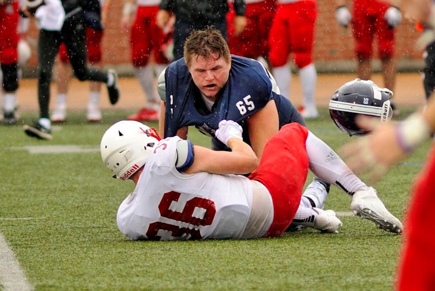 St. F.X. X-Men offensive lineman Gregor MacKellar loses his helmet in this battle with his Acadia opponent during an exhibition contest, Aug. 18, at Oland Stadium. Bryan Kennedy