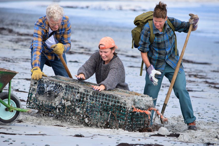 Terry McLaughlin (from left), Shayla Nickerson and Nelson work to dig a lobster trap buried in the sand at the Crow Neck Beach in East Baccaro during a shoreline cleanup on Sept. 25.