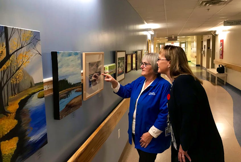 Simone Sweeney (left) of the Yarmouth Hospital Auxiliary and Lynn Burke-Newell, administrative assistant, nursing administration, at the Yarmouth Regional Hospital, get a closer look at one of the pieces in a new art project at the Yarmouth hospital, where an art gallery has been set up in the first-floor corridor connecting buildings B and C.