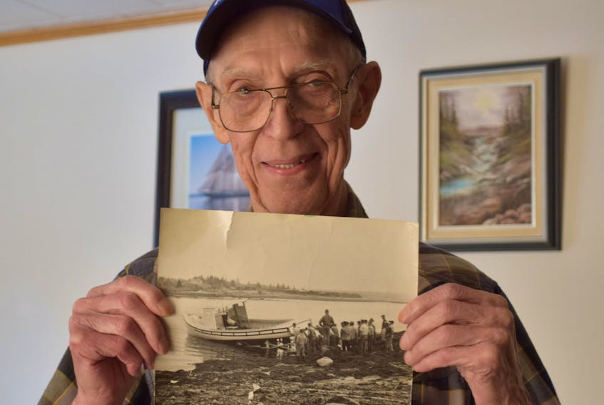 Roland  DesChamp Sr. holds a photo of the first boat launched in 1963 by DesChamp and Jackson boatbuilders. KATHY JOHNSON