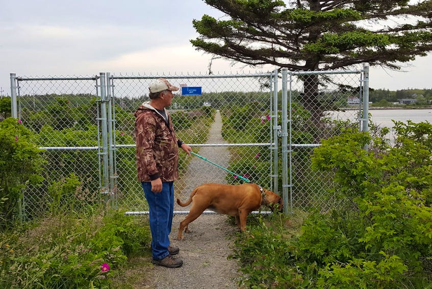 A man and his dog stop by the chain link fence and gate blocking access to Lockeport’s historic trestle bridge walking trail before it was vandalized.