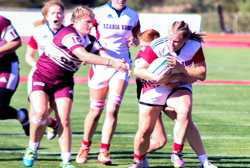 Tomi McCarthy clutches the rugby ball as she pulls away from her opponents during a university rugby game between Acadia and Saint Mary’s.