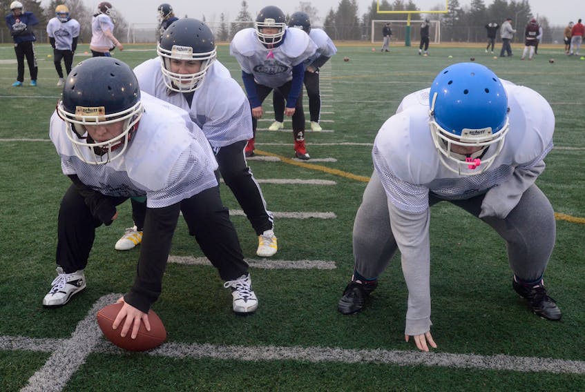 The Island Demons centre Jacky Buell prepares to snap the ball to quarterback Alexie Mireault as left guard Lindsay Payne waits for the play to start during Thursday’s practice at the Terry Fox Sports Complex.