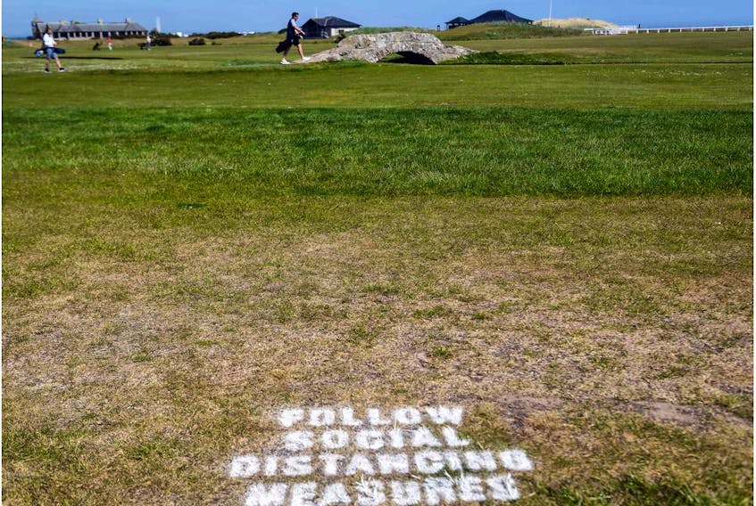 A golfer crosses the iconic Swilcan Bridge with a sign on the grass reminding golfers to respect social distancing measures at The Old Course in St Andrews, Scotland on May 29, 2020, as the Scottish Government eases lockdown restrictions during the novel coronavirus COVID-19 pandemic. (Photo by Andy Buchanan / AFP)