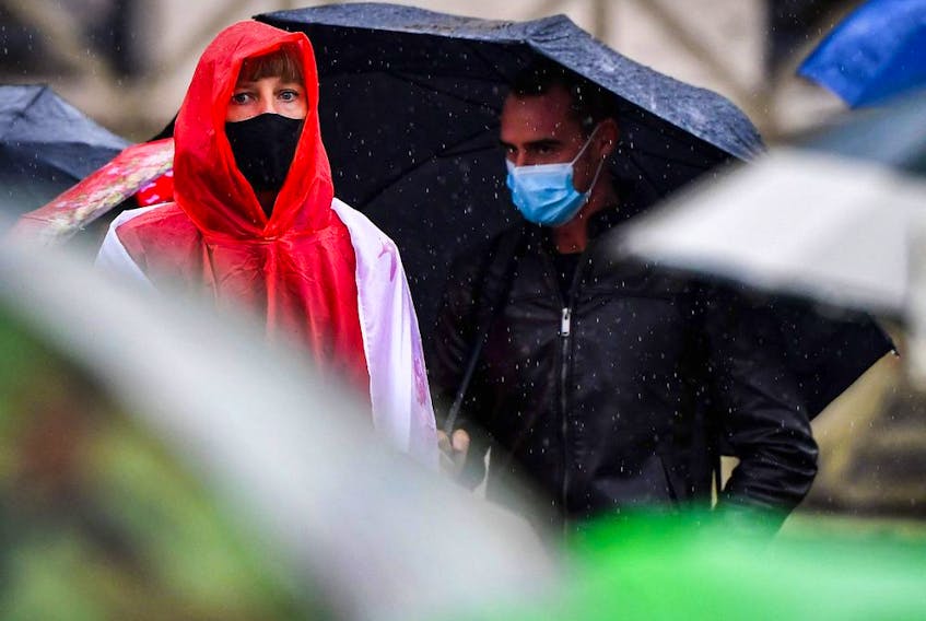 People wearing face masks, and protecting themselves from the rain.