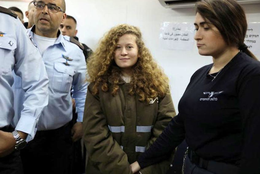 Palestinian teen Ahed Tamimi enters a military courtroom escorted by Israeli security personnel at Ofer Prison, near the West Bank city of Ramallah, January 15, 2018. 

(REUTERS/Ammar Awad)