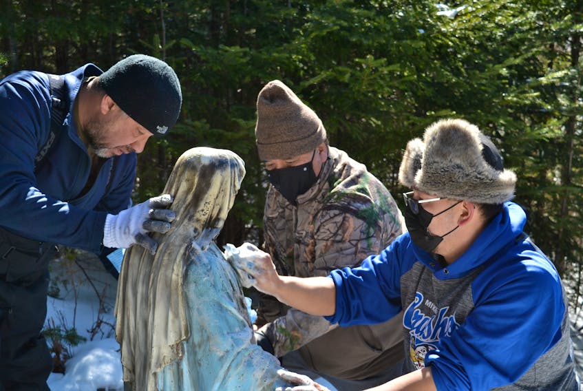 Fred Sylliboy, Walter Denny and Pierre Gould clean the blackened statue of the Blessed Mother. Denny found the statue in flames on Friday afternoon, and volunteers spent much of Saturday trying to repair the damage. ARDELLE REYNOLDS/CAPE BRETON POST 