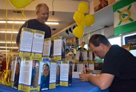 Weather enthusiast Frankie MacDonald, right, signs one of his bobbleheads for Robert Bowes during a session on Thursday morning at the Discount Dollar Store in Whitney Pier.