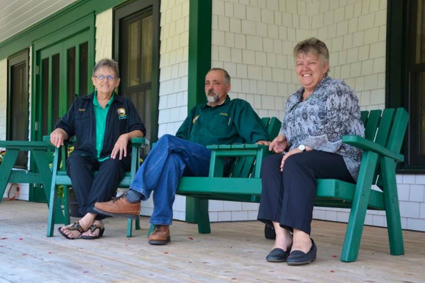 Ruth Bowe, Charlie Richard, and Val Richard sit on Adirondack chairs on the front verandah of the new Milford House lodge. It’s called the Richard and Bowe Verandah. “In recognition of their contributions to rebuilding of the lodge,” a sign reads.
