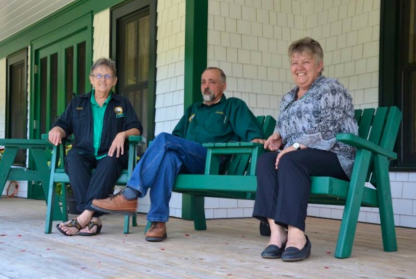 Ruth Bowe, Charlie Richard, and Val Richard sit on Adirondack chairs on the front verandah of the new Milford House lodge. It’s called the Richard and Bowe Verandah. “In recognition of their contributions to rebuilding of the lodge,” a sign reads.