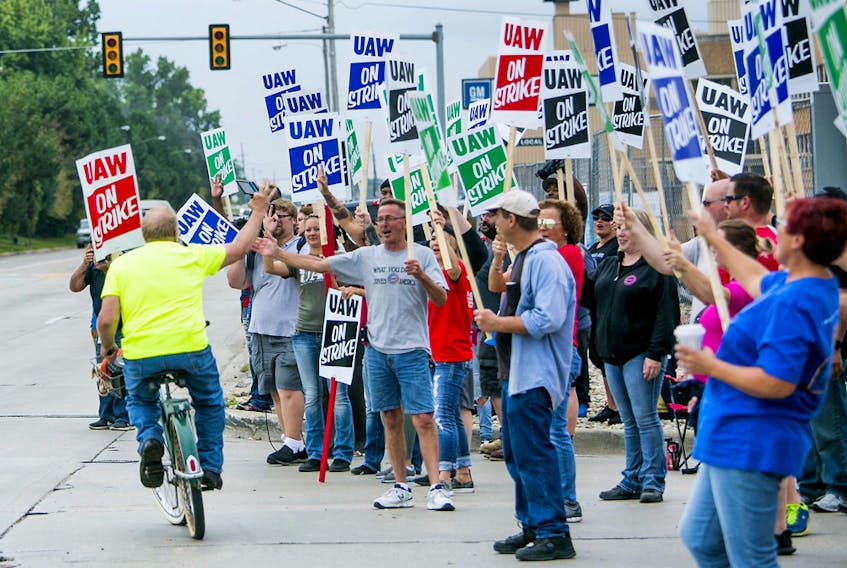  Demonstrators wave at a coworker cycling past during a United Auto Workers strike outside the GM assembly plant in Flint, Mich.