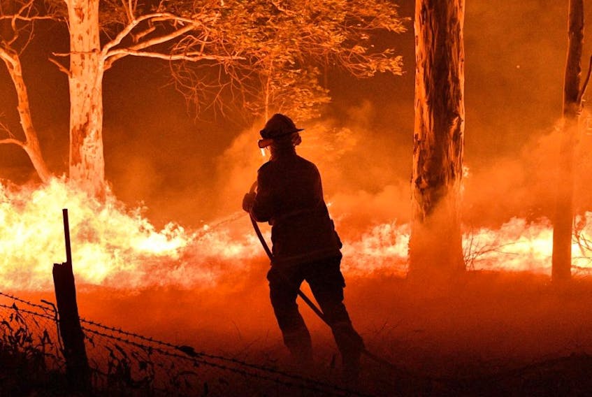 This picture taken on Dec. 31, 2019, shows a firefighter hosing down trees and flying embers in an effort to secure nearby houses from bushfires near the town of Nowra in the Australian state of New South Wales.