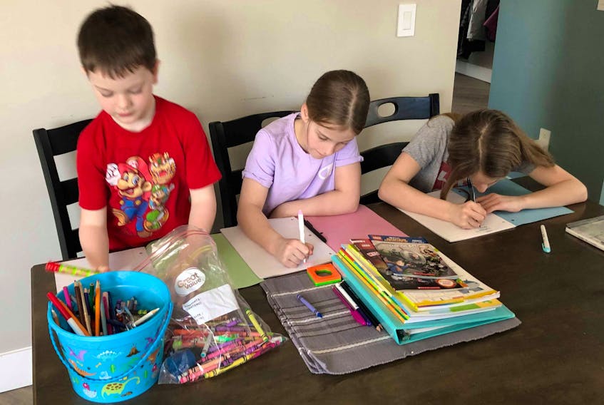 Max Hillier, six, and his sisters (from left) 10-year-old Marissa and 12-year-old Maggie, do school work at the kitchen table of their Sydney River home on March 22. Like many parents in Cape Breton, their mother Shelley is filling in as teacher during the two-weeks schools across the province are closed due to COVID-19 precaution measures. Shelley said she has created a schedule for her children that involved two-hours of school work, baking and an hour outside, which takes up about four hours of their day. The rest is free-time. Many parents are sharing on social media how they are teaching their children while school is out. Along with reading and writing, some include housework, cooking and art as lessons their children are getting during this time. CONTRIBUTED 