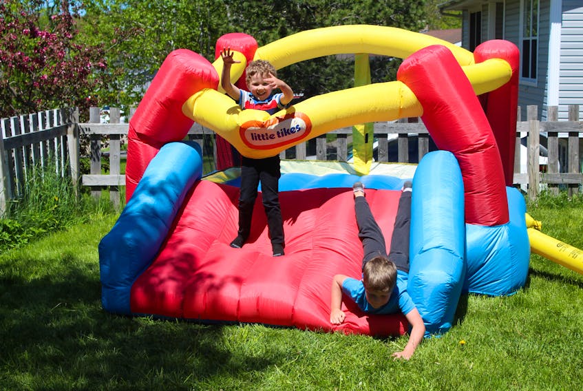 Five-year-old Colby MacNeil, left, throws himself into the wall of the family's bouncy structure as his seven-year-old brother Kaiden lands at the bottom of the slide after a few jumps. The boys were making good use of the toy in the front yard of their Sydney home on Wednesday. NICOLE SULLIVAN/CAPE BRETON POST