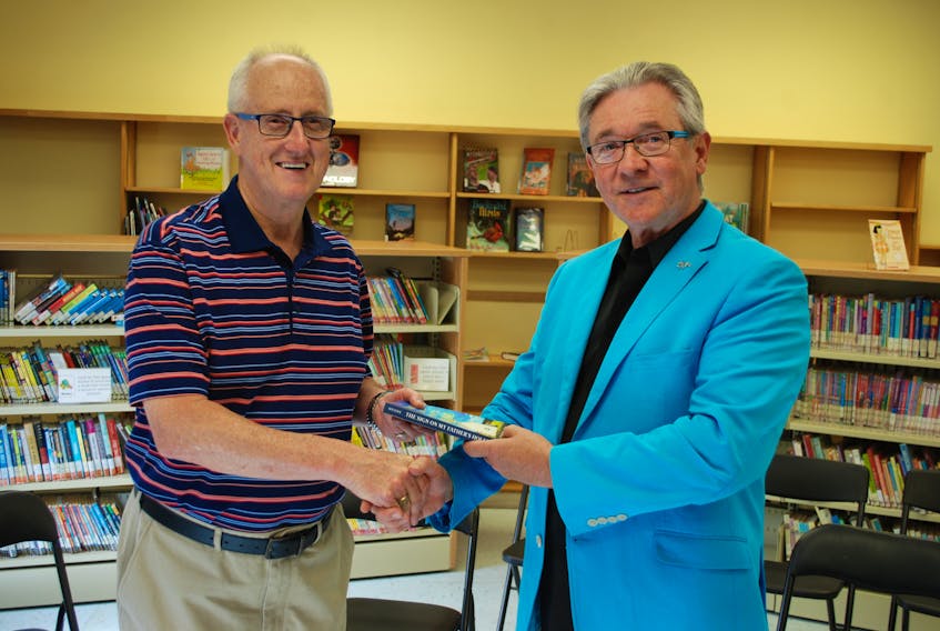 Clarenville Mayor Frazer Russell (left) accepts a copy on behalf of the town of “The Sign on My Father’s House” from author Tom Moore.