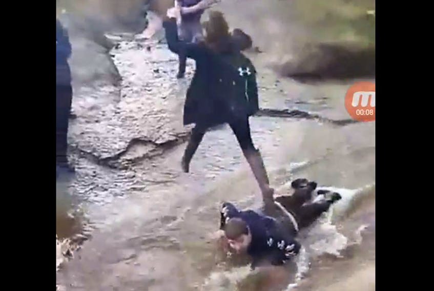 This Facebook video screen grab shows a teen lying in a stream and young girl walking on him. - Facebook