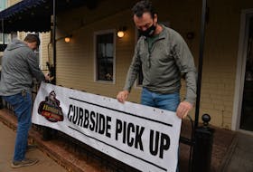 Jeff Sinnott, right, co-owner of Hunter's Ale House in Charlottetown, and Mike Savidant of Sign Craft put up a sign for take-out and curbside pick up orders after the province temporarily shut down restaurant dining rooms on Sunday.
