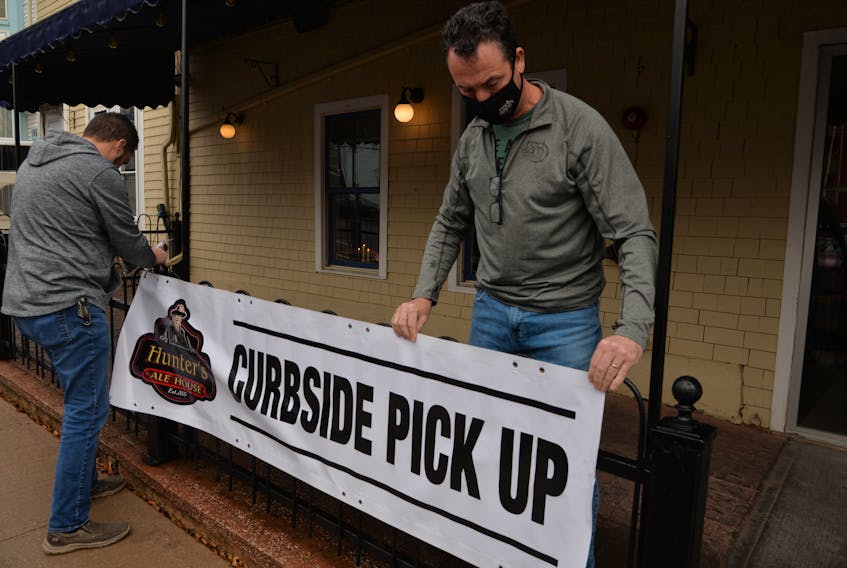 Jeff Sinnott, right, co-owner of Hunter's Ale House in Charlottetown, and Mike Savidant of Sign Craft put up a sign for take-out and curbside pick up orders after the province temporarily shut down restaurant dining rooms on Sunday.