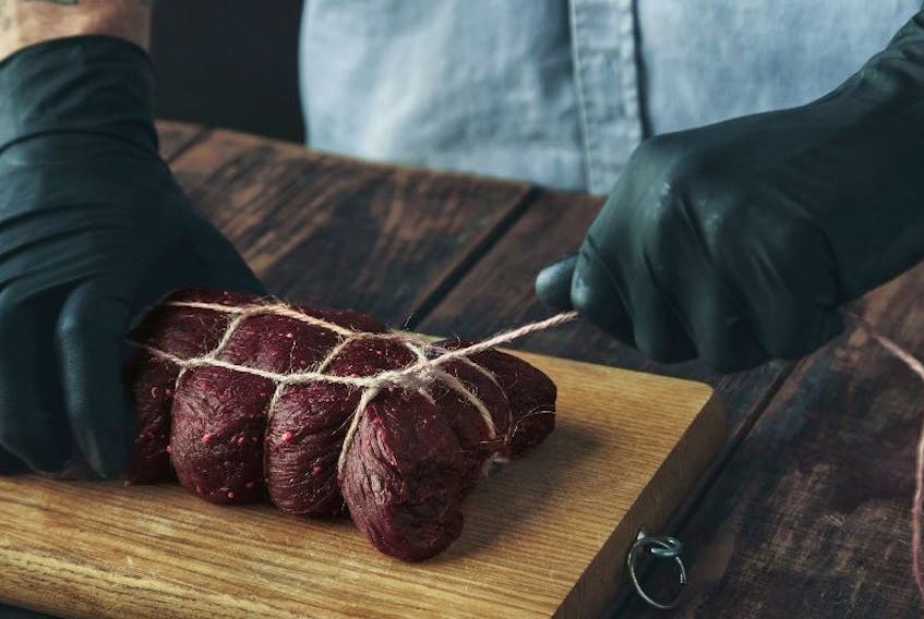 A butcher ties a piece of meat with craft rope to smoke it on a wooden aging table.