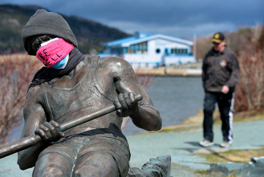 Someone has placed a mask on the Regatta rower statue on the shore of Quidi Vidi Lake. The Quidi Vidi boathouse is in the background.