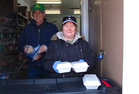 Jerry Pocius, left, and Florence MacNeil hold up takeout meals from Loaves and Fishes in Sydney, which are being served to clients while the dining area is closed. NICOLE SULLIVAN/CAPE BRETON POST