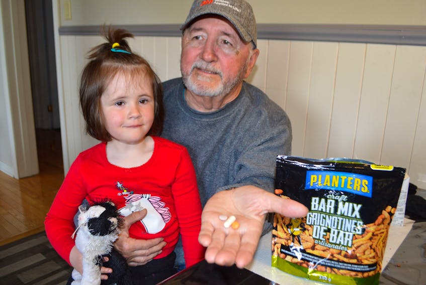 Stan Peach of Glace Bay sits with his four-year-old great-granddaughter Summer, holding pills they found while eating some Planters Craft Bar Mix at home on Sunday. Peach said officials of Johnvince Foods in Ontario – manufacturers of the product — are harassing him for the pills but he’s not turning them over until they are analyzed and has contacted the Canadian Food Inspection Agency for help. Sharon Montgomery-Dupe/Cape Breton Post