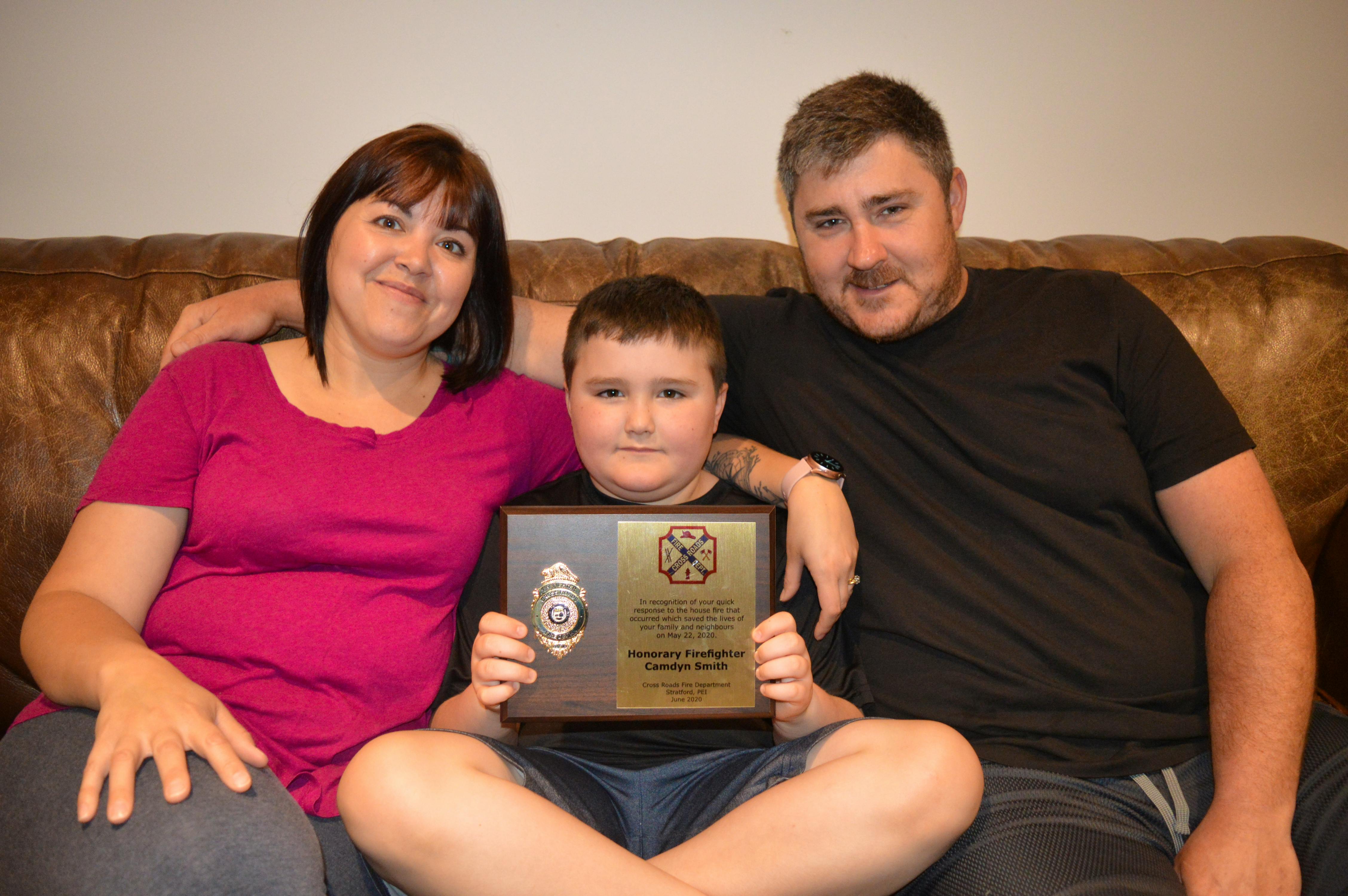 Nine-year-old Camdyn Smith holds the plaque given to him by the Cross Roads Fire Department for his actions that saved the lives of his parents, Erin, left, and Jamie Smith, and their neighbours. 