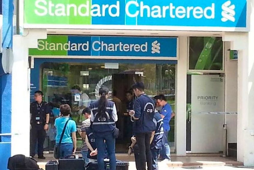 Singapore police are seen here at the Standard Chartered Bank's Holland Village Park branch in Singapore on July 7, 2016 after the bank was robbed. David James Roach of River Ryan is a suspect in the robbery but the attorney general's office in Bangkok, Thailand rejected a request to extradite Roach to Singapore and Tuesday Roach was sentenced in a Thai court to 14 months in jail for violating money laundering and customs laws.