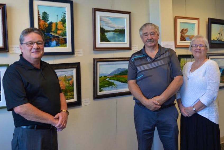 Harvey LeBlanc, manager of the New Waterford Credit Union, left, stands with artist Colonel MacLellan and his wife Jackie MacLellan on Friday. MacLellan’s first art show is on display at the New Waterford Credit Union Art Gallery on Plummer Avenue.