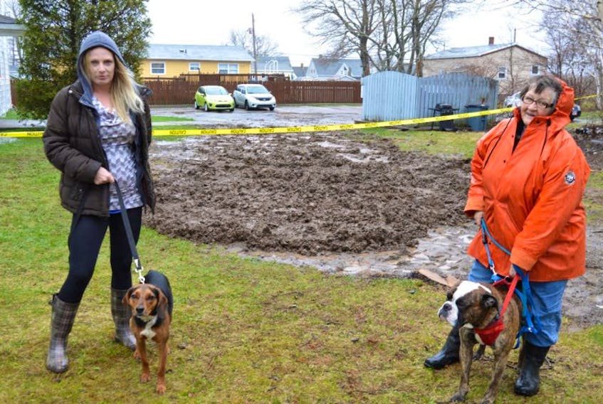 Jessie Bainbridge, left, with her dog Spartacus, and Cathy Crosby, with her dog Bubba, stand near their apartment complex on Dominion Street, Glace Bay, where a sinkhole was filled in on Thursday morning. Bainbridge and Crosby said residents are worried about their safety. The complex is owned by Metcap Living which has an office in Dartmouth.