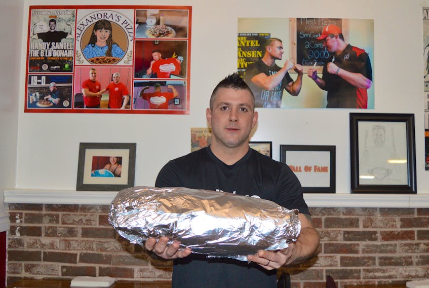 Alexandra's Pizza owner Justin Ayre holds a 12-pound donair at the Charlotte Street location on Tuesday. The shop is offering $2,000 — $1,000 in cash and a $1,000 charitable donation — to anyone who can consume the colossal combination of spicy shaved beef, tomatoes, onions and sweet garlic sauce, which is wrapped up in a pita the size of a large pizza, in 90 minutes. On the wall in the background are Joel Hansen and competitive eating champion Randy Santel, who both completed the pizza shop’s previous six-pound donair challenge.