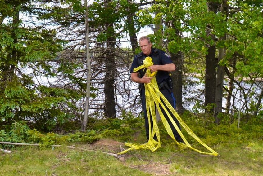 A Cape Breton Regional Police officer removes crime scene tape from the woods near Union Presbyterian Church in Albert Bridge on Wednesday. A passerby discovered the body in the water near the church at approximately 1:40 p.m., days after police formally called off the search for missing Albert Bridge man Murray Reid, 56, who reportedly fell from his boat into the river near Mira Ferry Lane in Albert Bridge on June 5.