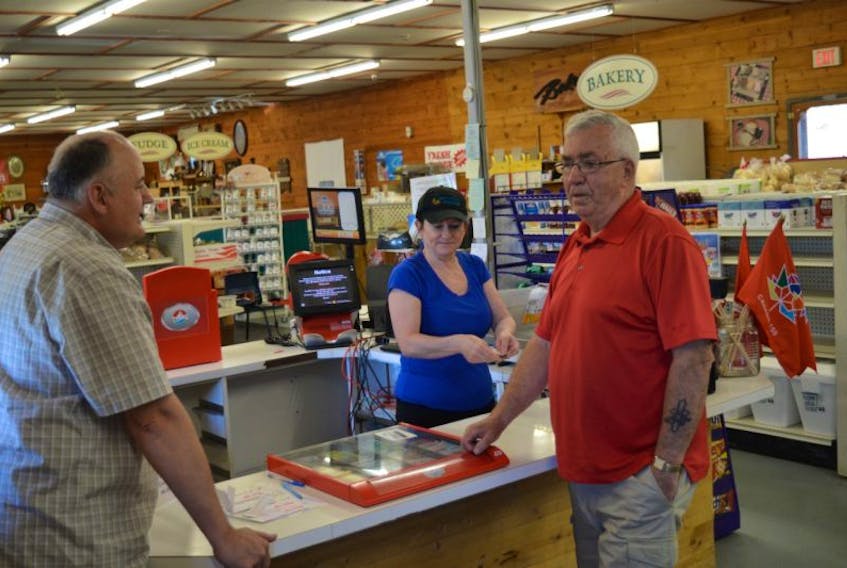 Brett LeBlanc, right, stands at the counter of his store, the Celtic Country Market in Bras d’Or, with employee Denise Bushell and customer John Young.