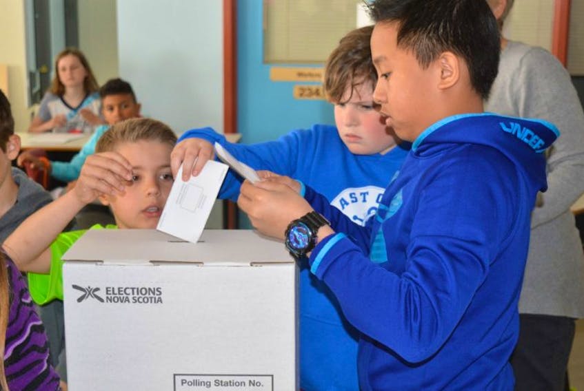Three students get ready to drop their ballots into the voting box at Brookland Elementary School in Sydney as part of the Student Vote program.