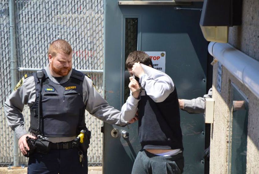 Thomas Joseph Smith, 26, of Sydney, shields his face from reporters’ cameras Monday as he was taken from the Sydney Justice Centre to the Cape Breton Correctional Centre. He is facing four charges in connection with a fatal hit and run in March that claimed the life of a 54-year-old Cheticamp man.