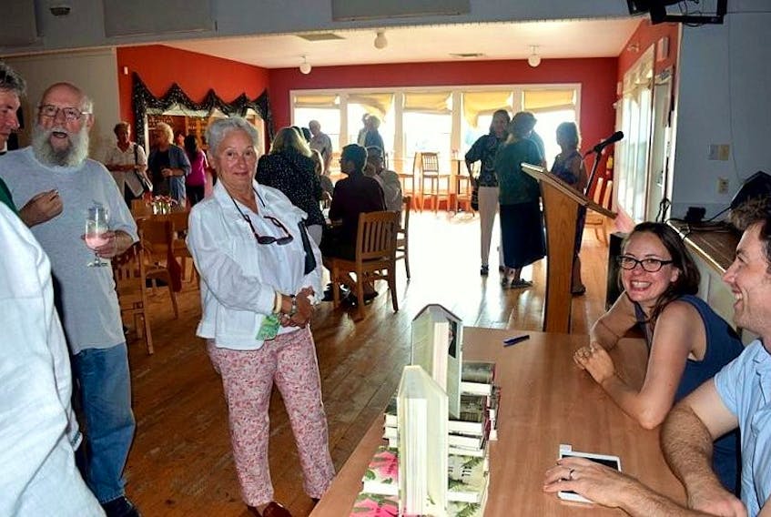 Author Sarah Faber, sitting at the table, smiles for the camera while autographing her debut novel “All is Beauty Now” during the book launch in Inverness on Aug. 13.